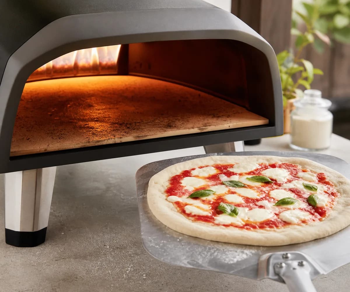 Baking surface recovering in a pizza oven while the next unbaked pizza waits on a peel.